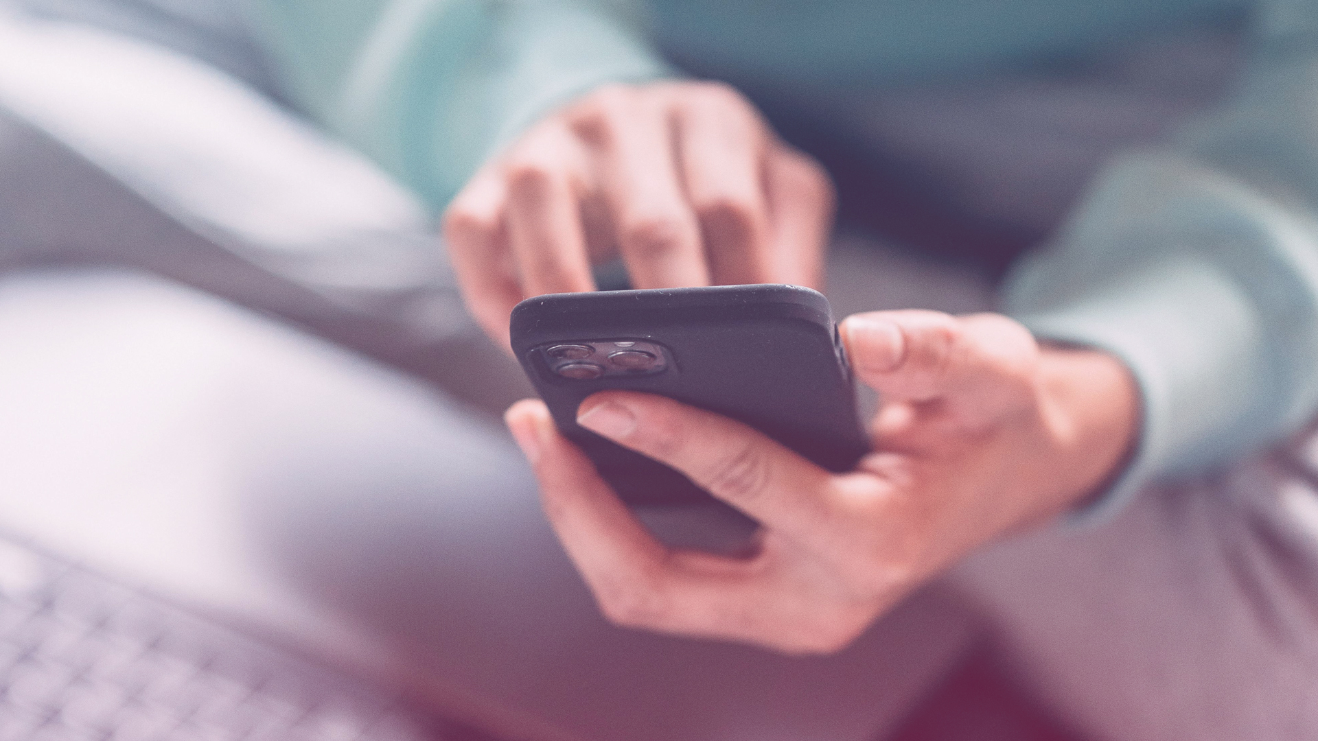 Was macht eine gute Website aus? Eine Person mit einem Laptop auf dem Schoß tippt am Smartphone.