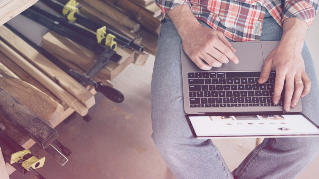 SEO für Handwerksbetriebe: Ein Mann sitzt neben einem Holzstapel und hat einen Laptop auf dem Schoß.